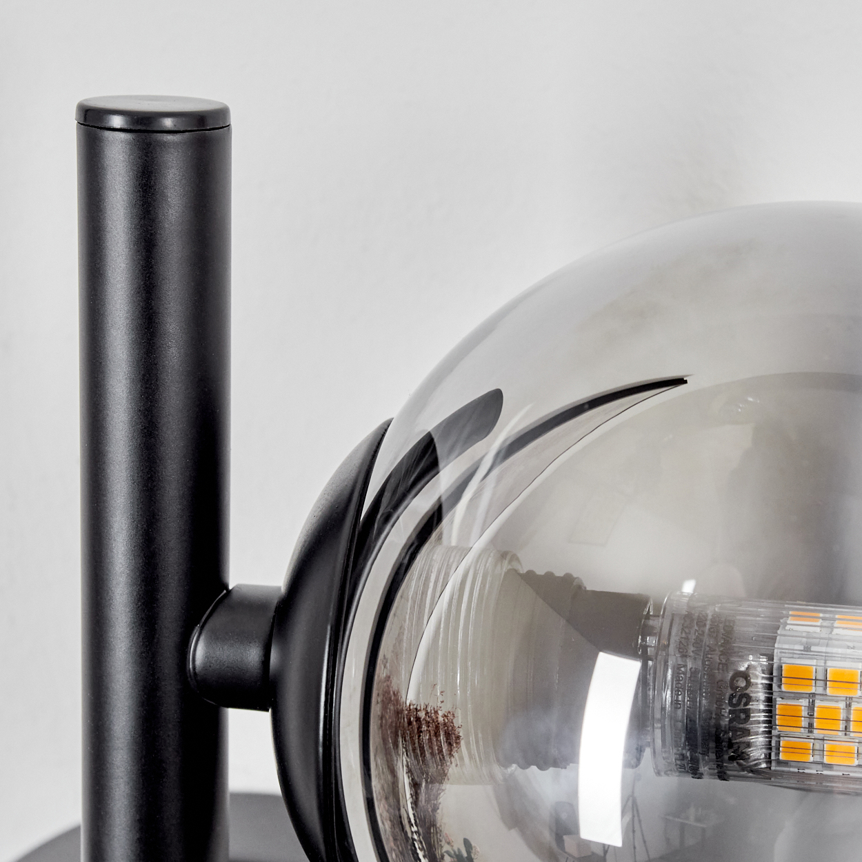 Nahaufnahme einer Glaskugelleuchte mit einer orangefarbenen LED-Glühbirne und einem schwarzen Metallrahmen.