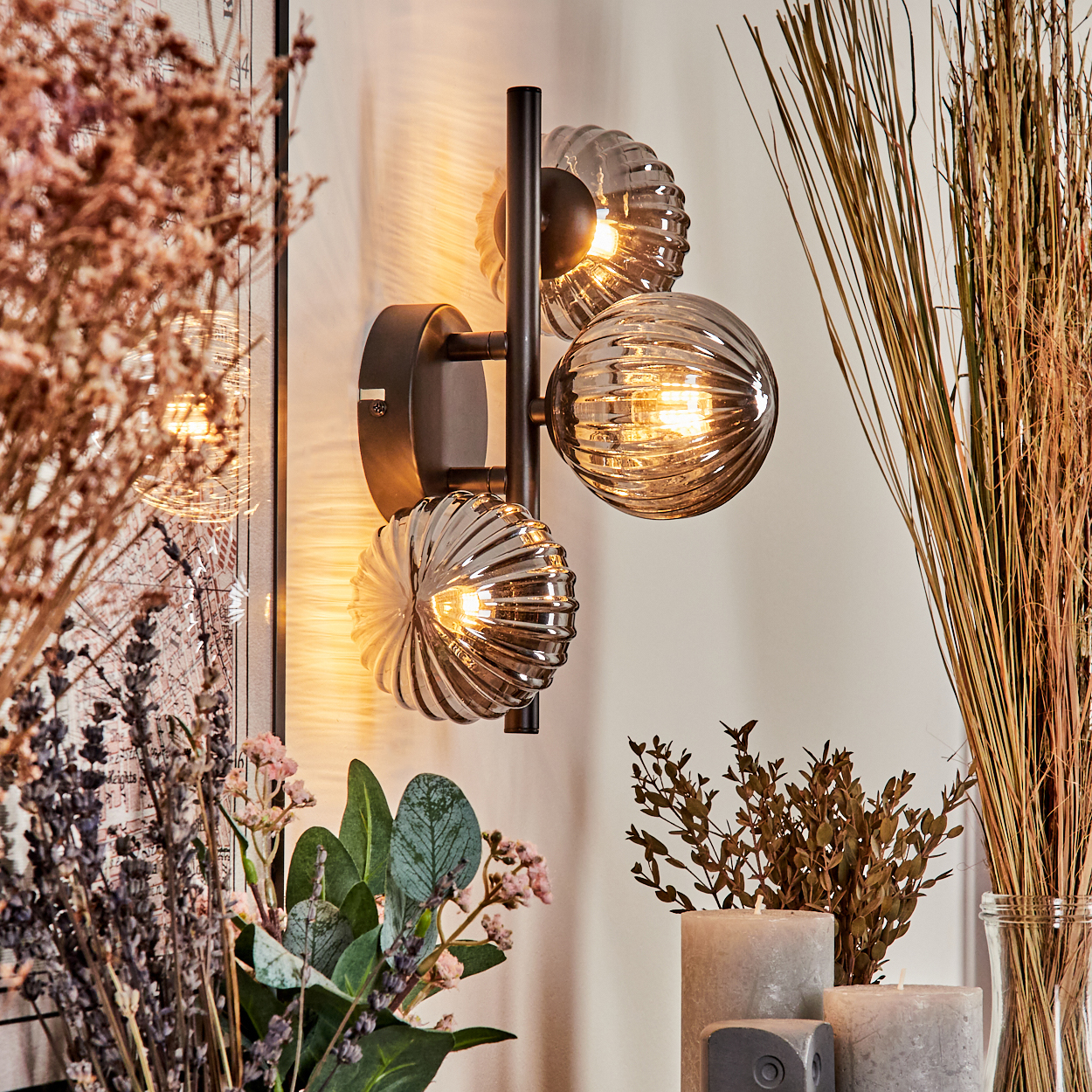 Eine Wandleuchte mit drei kugelförmigen Lichtern, Trockenblumen und Kerzen.