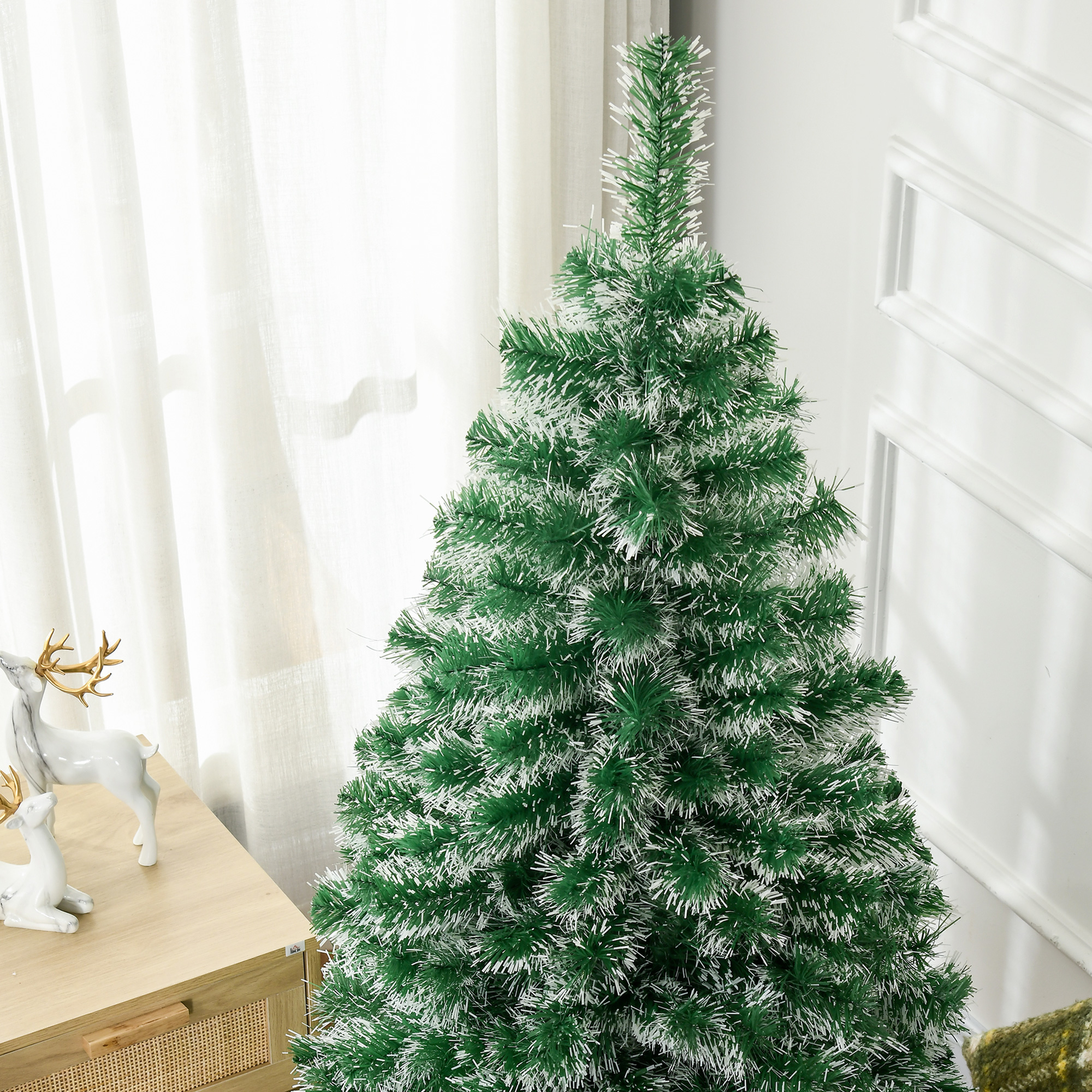 Ein grüner Weihnachtsbaum mit weißen, flauschigen Verzierungen. Er steht vor einer weißen Wand.
