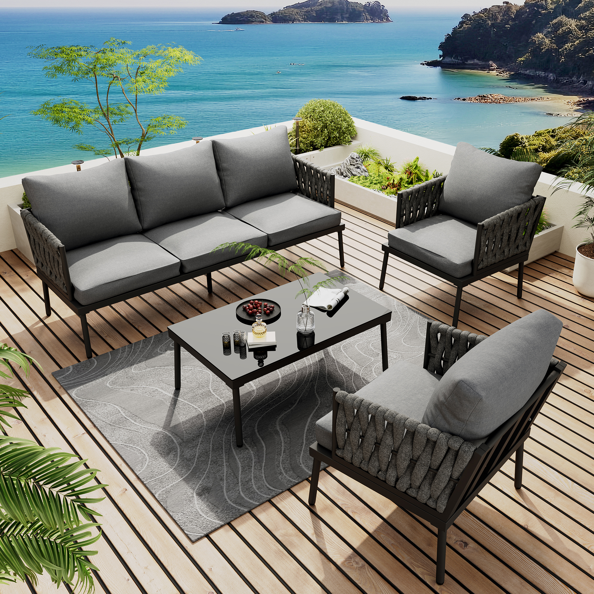 Outdoor-Terrassenset mit Sofa, zwei Sesseln und einem Tisch. Graue Kissen und schwarze Rahmen, auf einem Holzdeck mit Meerblick.