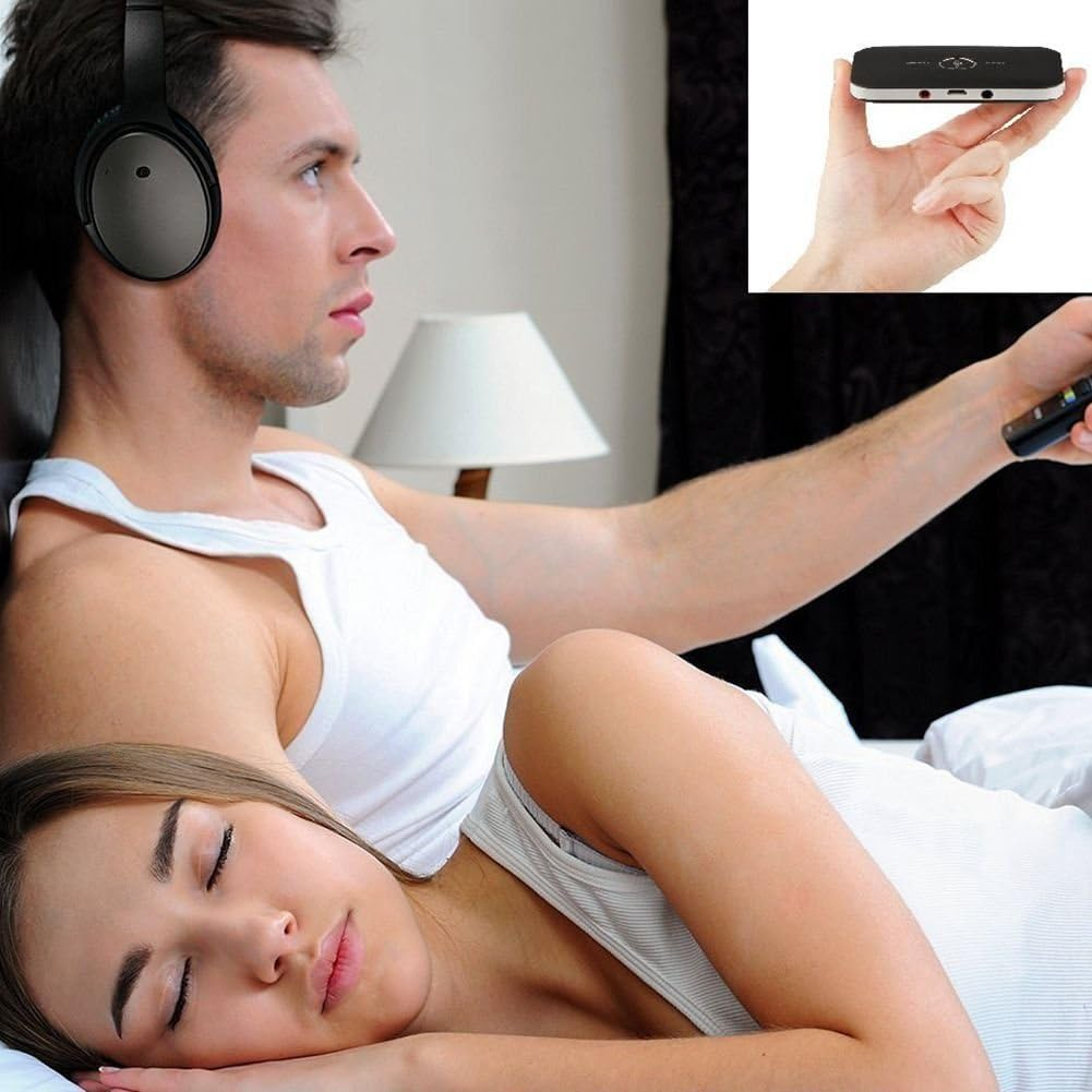 Ein Mann mit Kopfhörern sieht fern, während eine Frau im Bett schläft. Ein Gerät wird in der Hand gehalten.