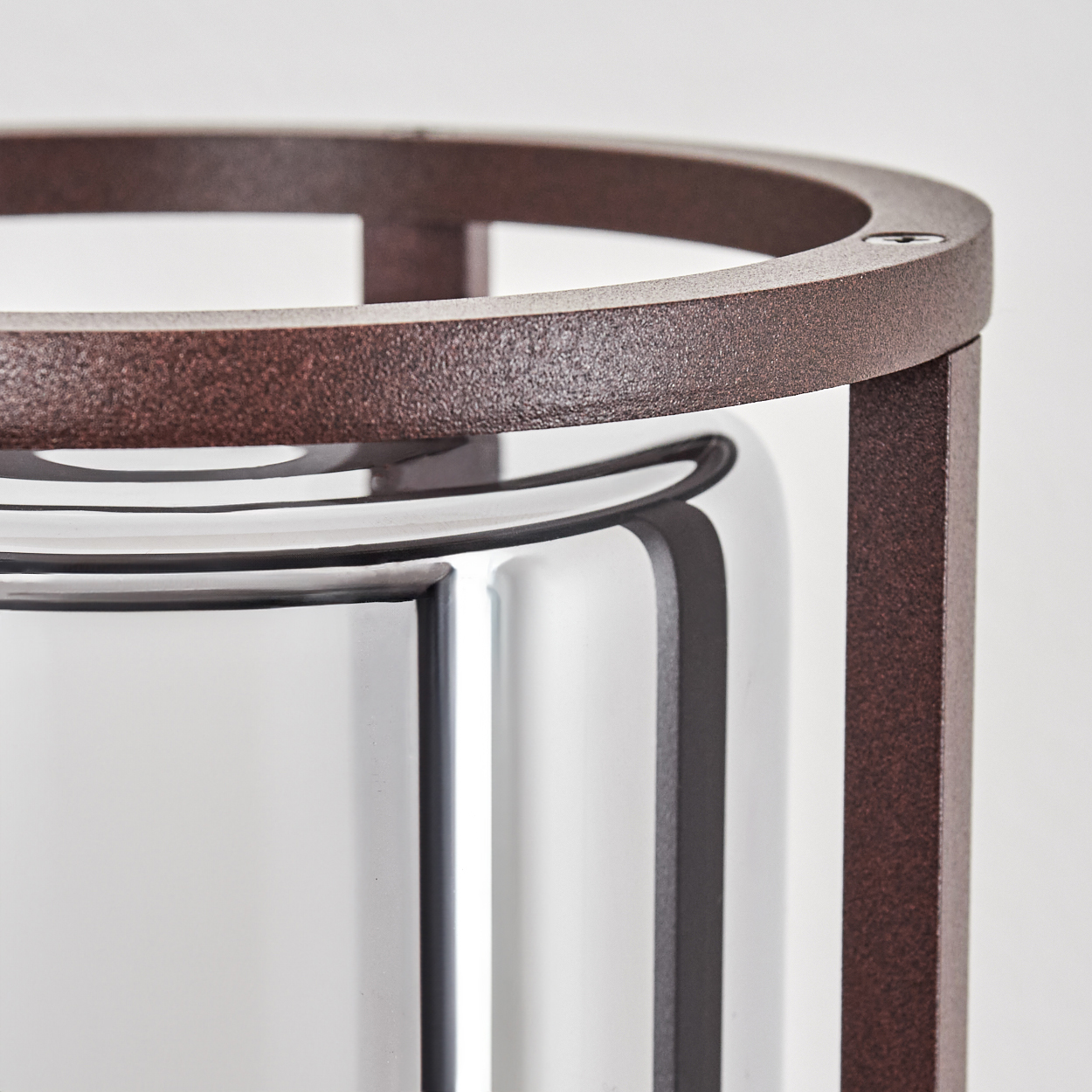 Nahaufnahme einer Wandleuchte, die den braunen Metallrahmen und das zylindrische Glas zeigt.