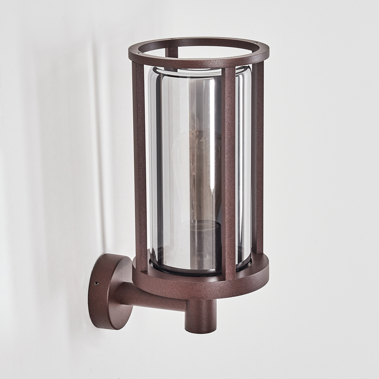 Braune, zylindrische Außenwandleuchte mit klarem Glasschirm und Metallrahmen.