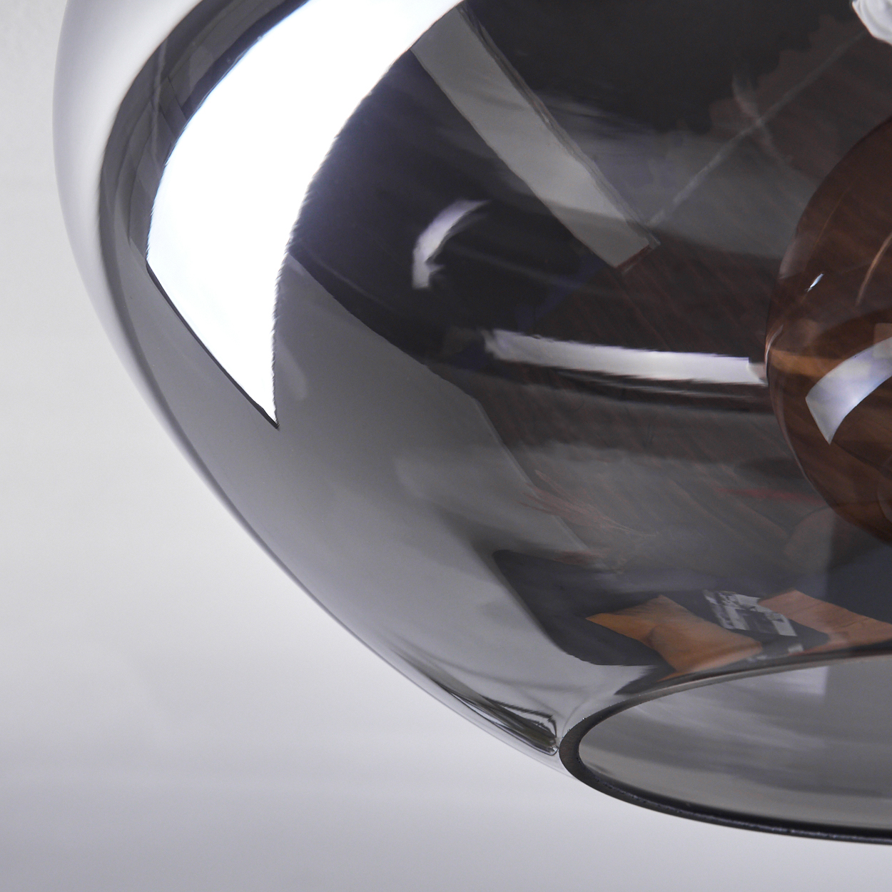 Nahaufnahme einer grauen Glasdeckenleuchte. Die Lampe reflektiert Licht und den Raum.