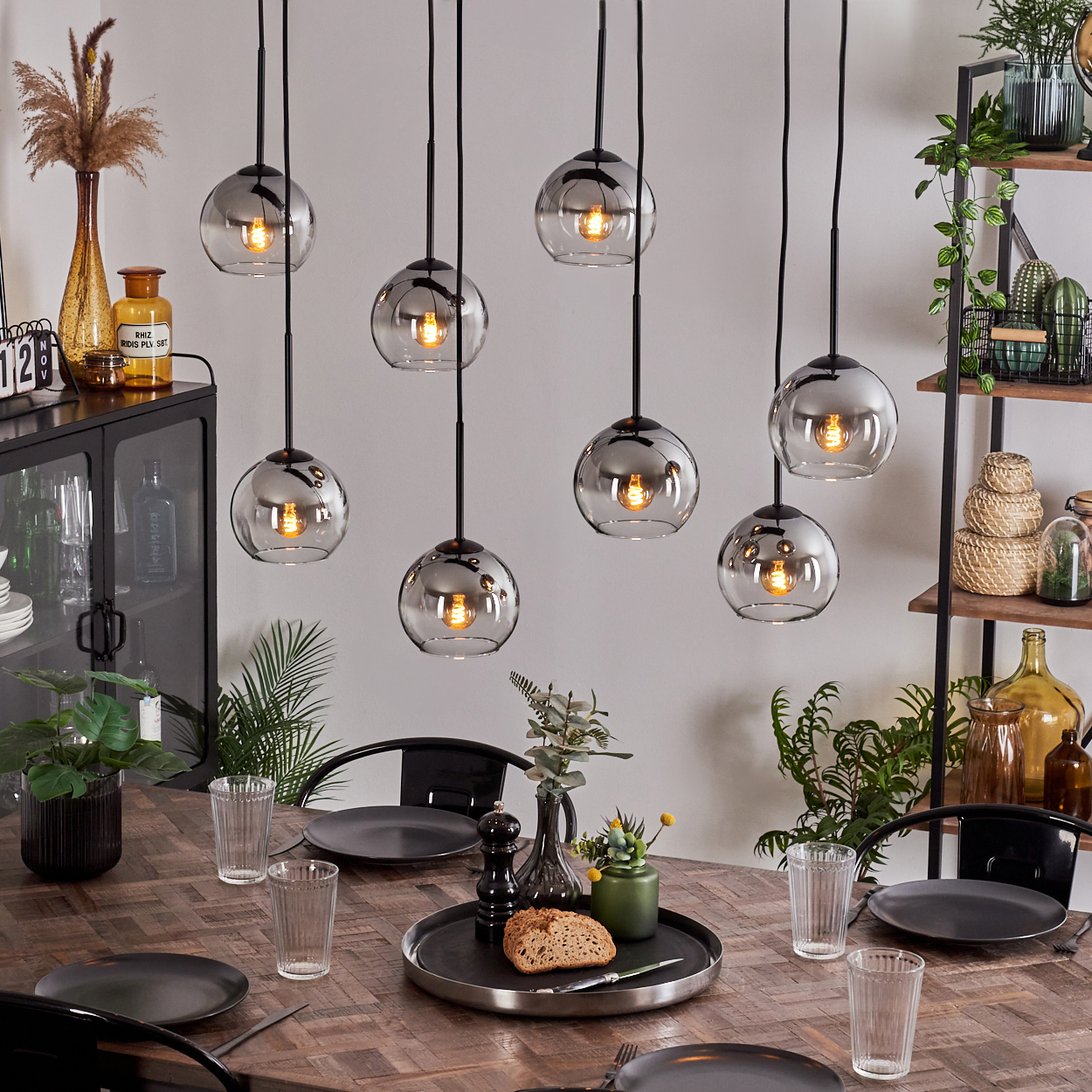 Ein Esszimmer mit einem Holztisch, acht Hängeleuchten und verschiedenen Dekorationen. Pflanzen sind ebenfalls sichtbar.