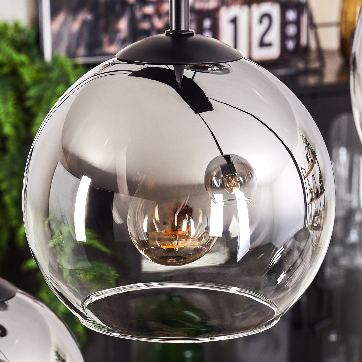 Nahaufnahme einer kugelförmigen Glaslampe mit einer Glühbirne im Inneren. Die Lampe spiegelt die Umgebung wider.