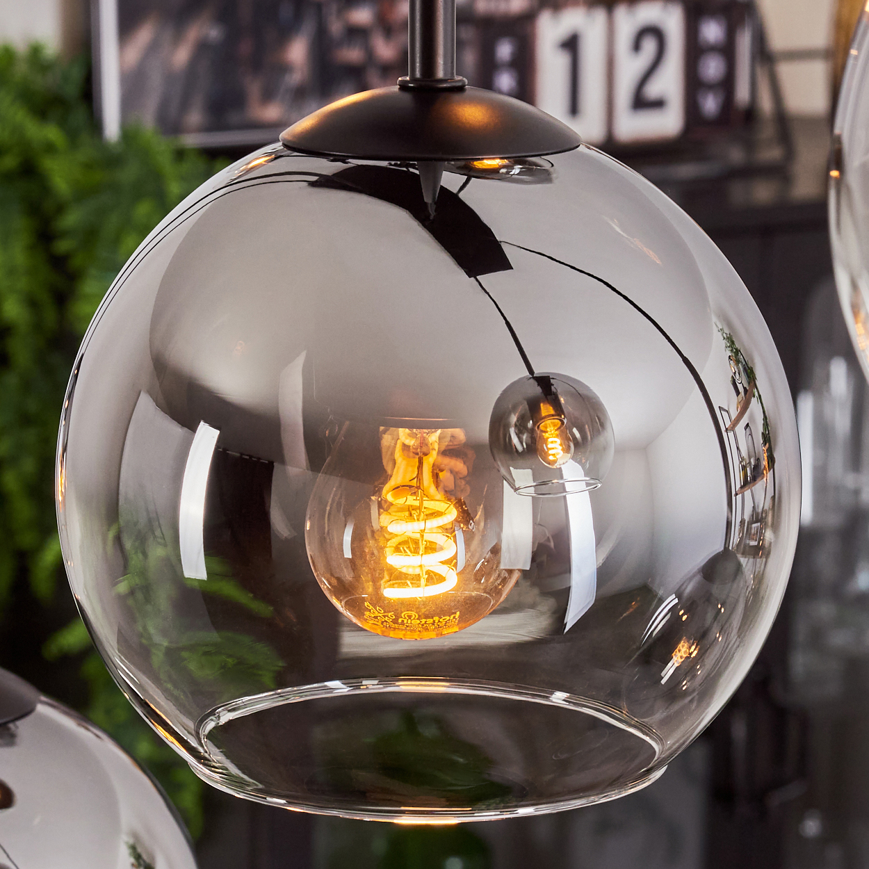 Nahaufnahme einer modernen Kugel-Pendelleuchte mit klarem Glasschirm und sichtbarer Glühbirne.