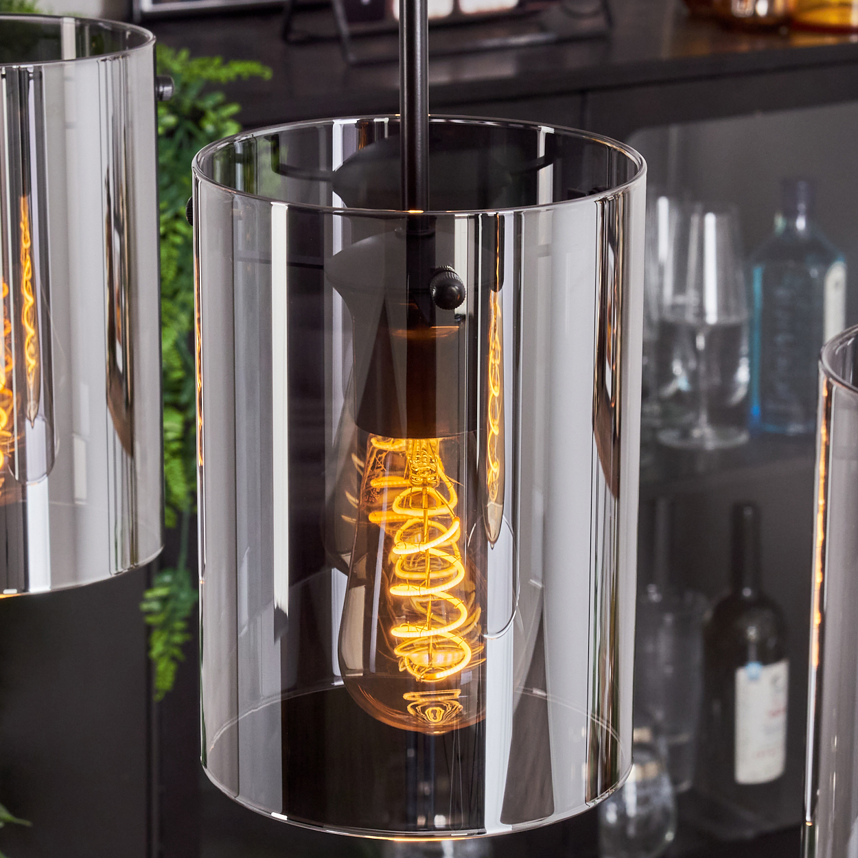 Nahaufnahme von drei Pendelleuchten mit zylindrischen, verspiegelten Glasschirmen und sichtbaren Wendelbirnen.