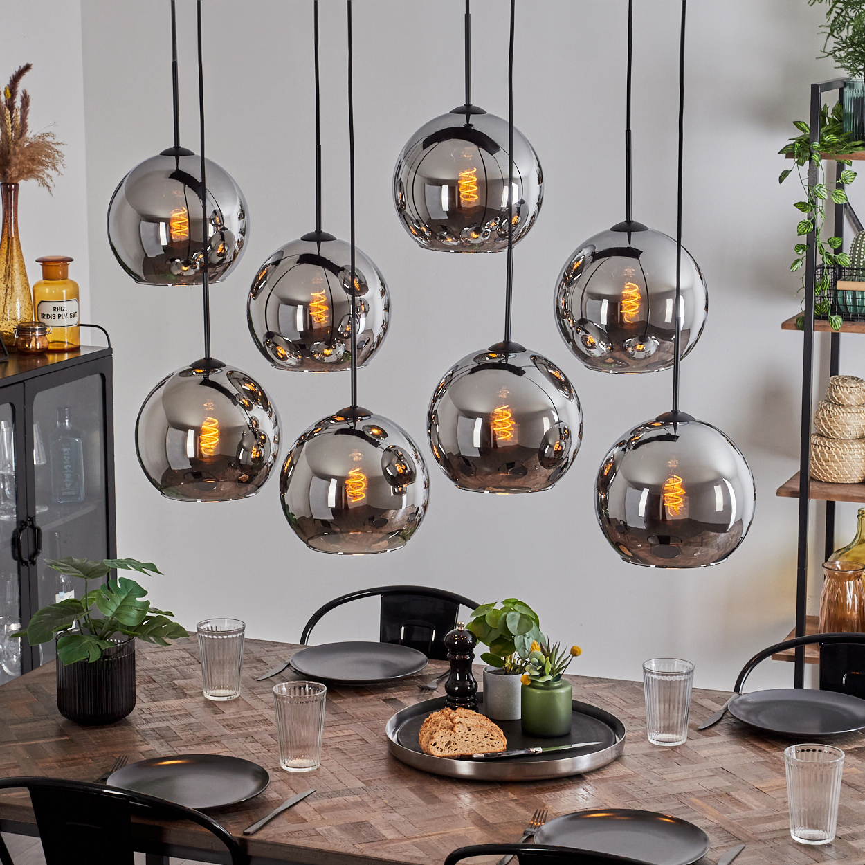 Esszimmer mit acht hängenden, kugelförmigen, verspiegelten Leuchten mit orangefarbenen Glühfäden über einem Holztisch.