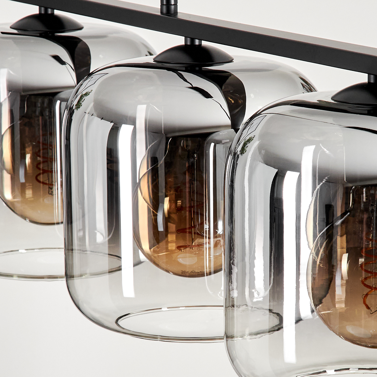 Nahaufnahme einer schwarzen Lampe mit drei Glühbirnen in klaren Glasschirmen. Weißer Hintergrund.