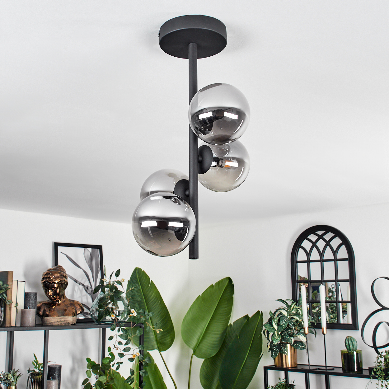 Eine schwarze Lampenhalterung mit vier kugelförmigen Glasschirmen, mit weißer Decke und verschiedenen Dekorationen.