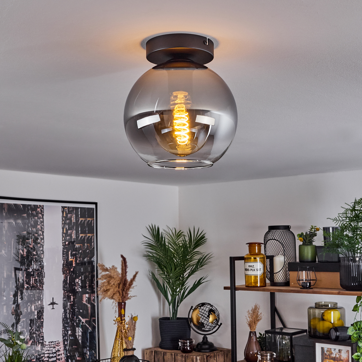 Eine Deckenleuchte mit kugelförmigem Glasschirm, einer sichtbaren Wendelglühbirne und einem Raum im Hintergrund.