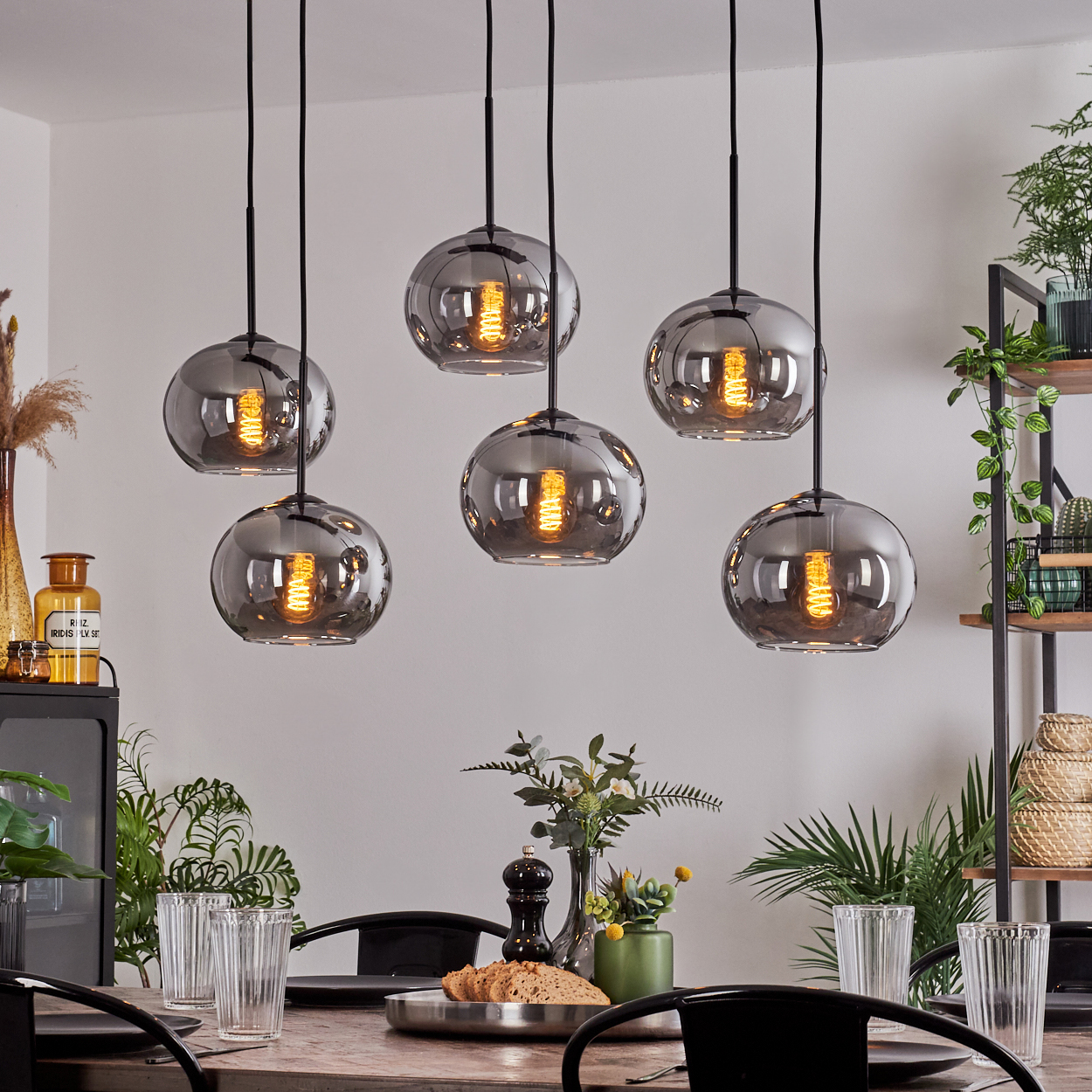 Ein Esszimmer mit sechs hängenden grauen Kugelleuchten über einem Holztisch, Pflanzen im Hintergrund.