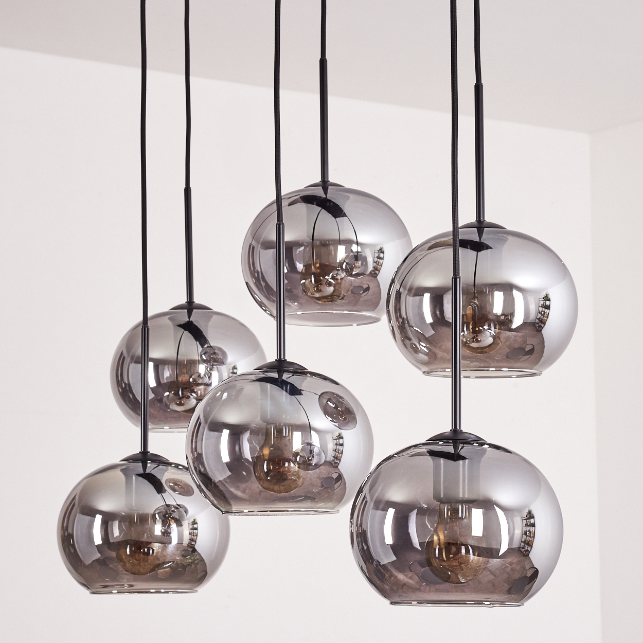 Sechs graue Glaskugel-Pendelleuchten hängen von einer Decke, jede mit sichtbaren Glühbirnen.