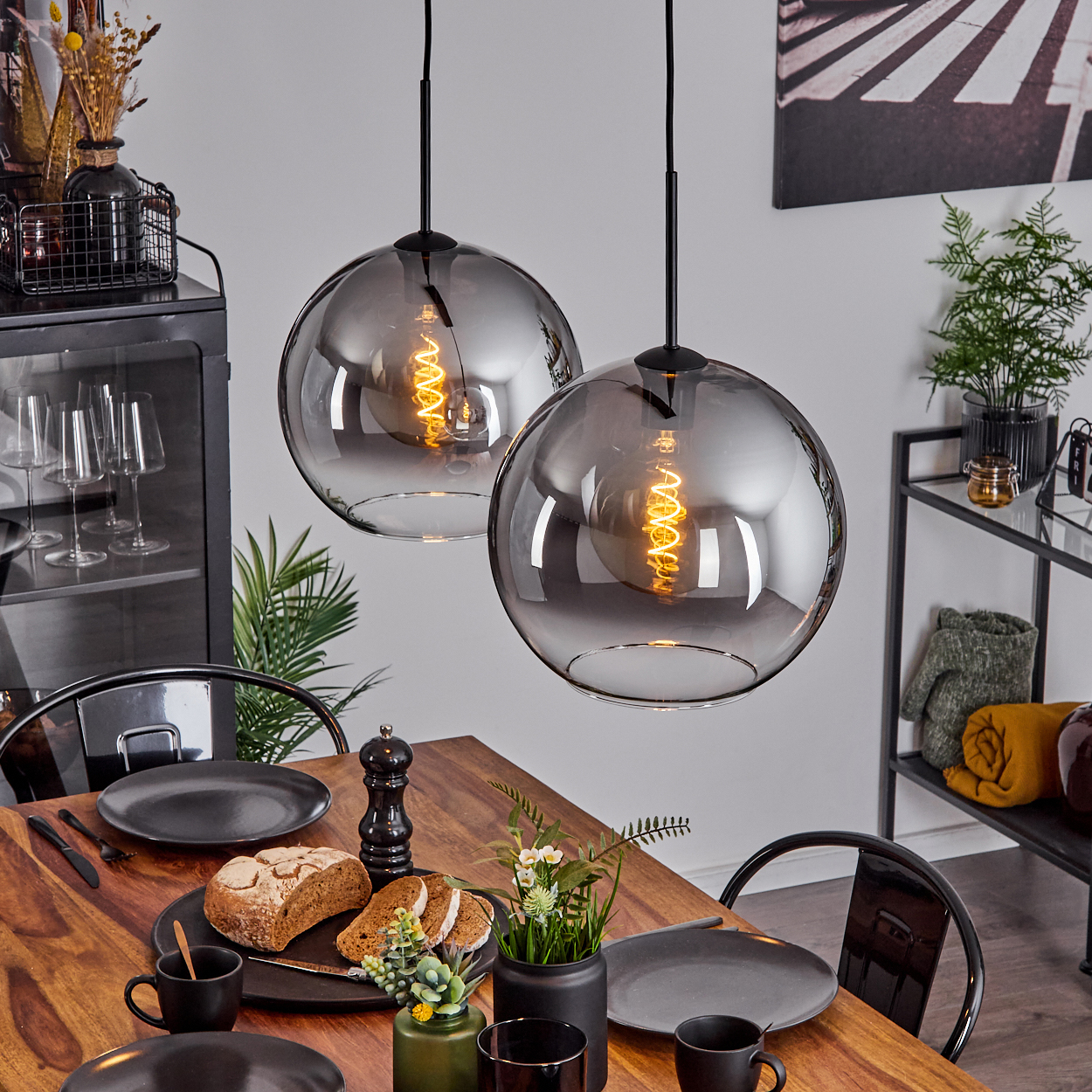 Zwei Hängelampen mit Glasschirmen und Wendelglühbirnen über einer Holztischdekoration.