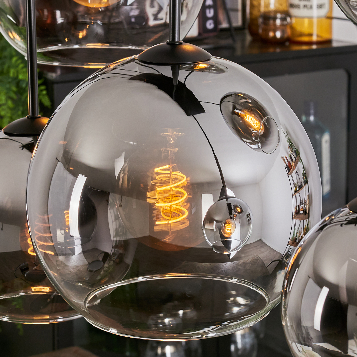Nahaufnahme einer Hängeleuchte mit Glasschirm und Wendelglühbirne, mit anderen Lampen im Hintergrund.