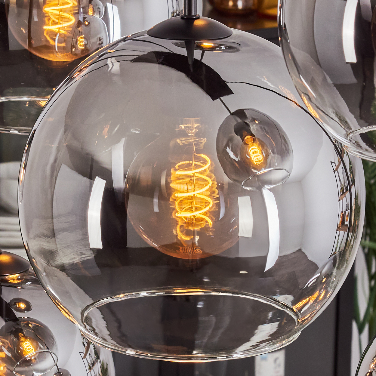 Nahaufnahme einer Hängeleuchte mit Glasschirm und Wendelglühbirne, mit anderen Lampen im Hintergrund.