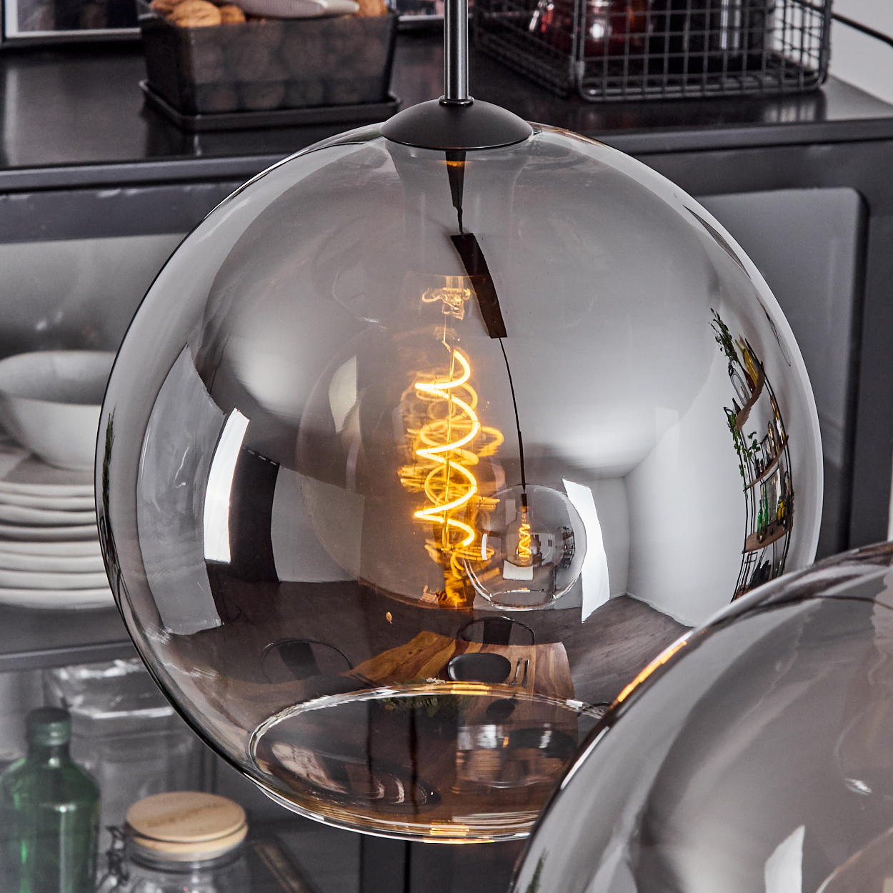 Nahaufnahme einer Hängeleuchte mit Glasschirm und Wendelglühbirne, mit anderen Lampen im Hintergrund.