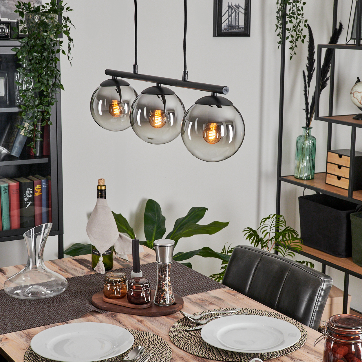 Esszimmer mit Holztisch, gedeckt mit Tellern und Kerzen. Drei Hängelampen mit grauen Glasschirmen.
