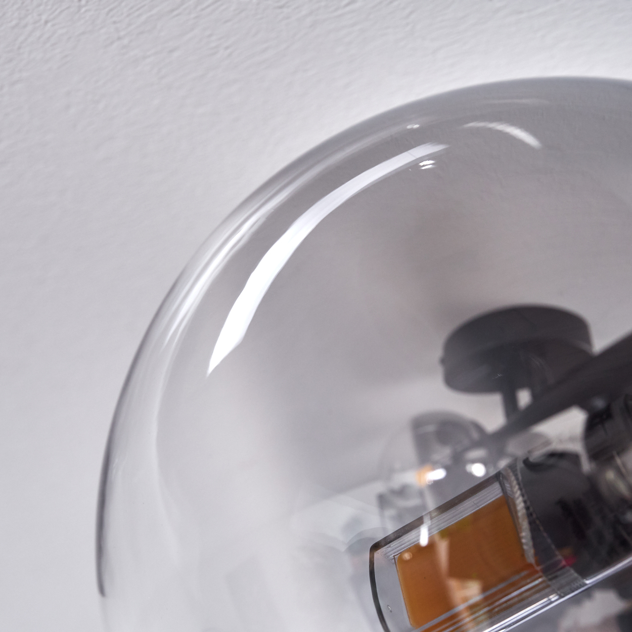 Nahaufnahme einer Pendelleuchte aus grauem Glas, die die Glühbirne und die Reflexion zeigt.