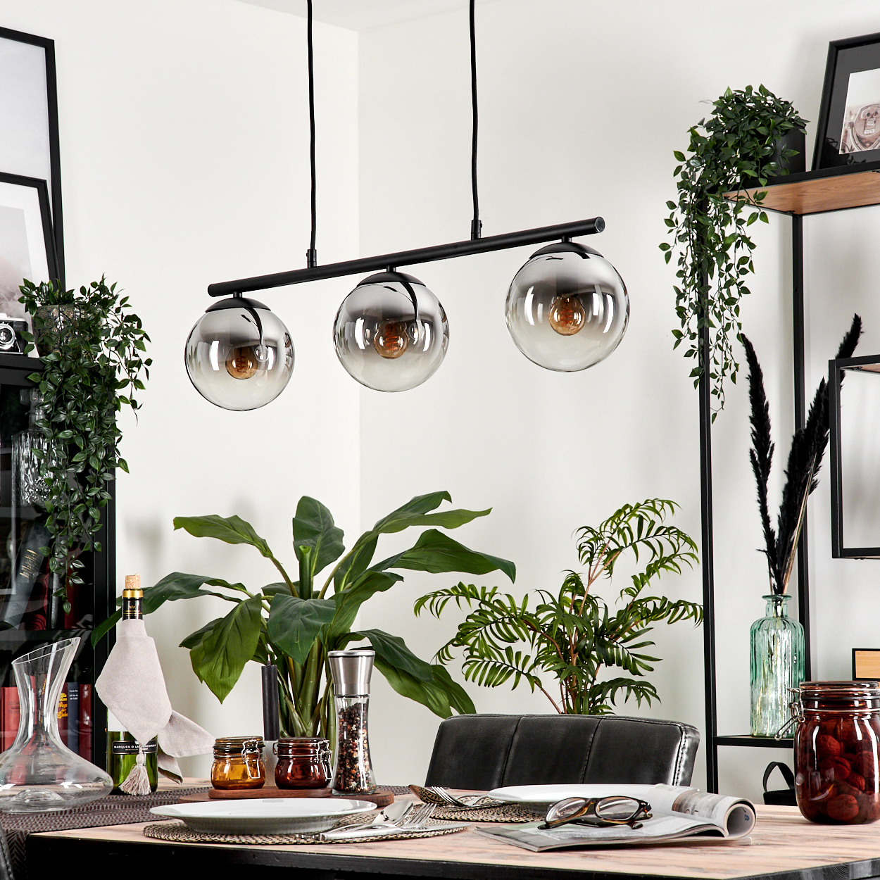 Esszimmer mit Holztisch, Pflanzen und Gläsern. Drei Hängelampen mit grauen Glasschirmen.