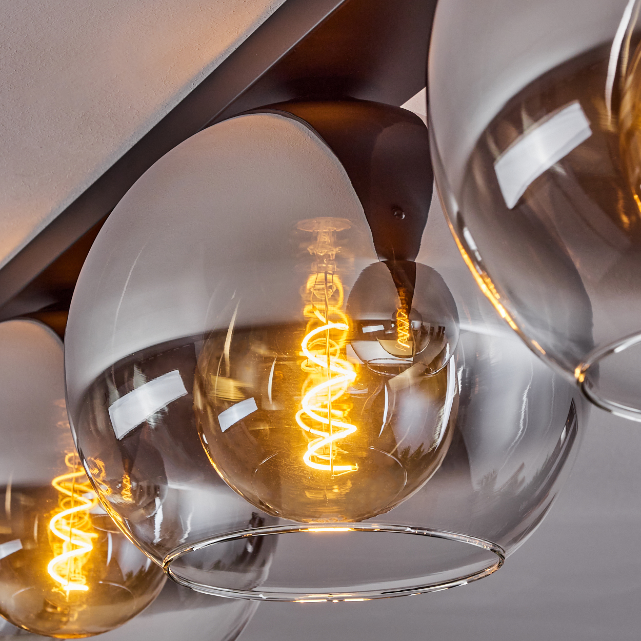 Nahaufnahme einer Leuchte mit drei kugelförmigen Glasschirmen. Jeder Schirm hat eine leuchtende, spiralförmige Glühbirne.