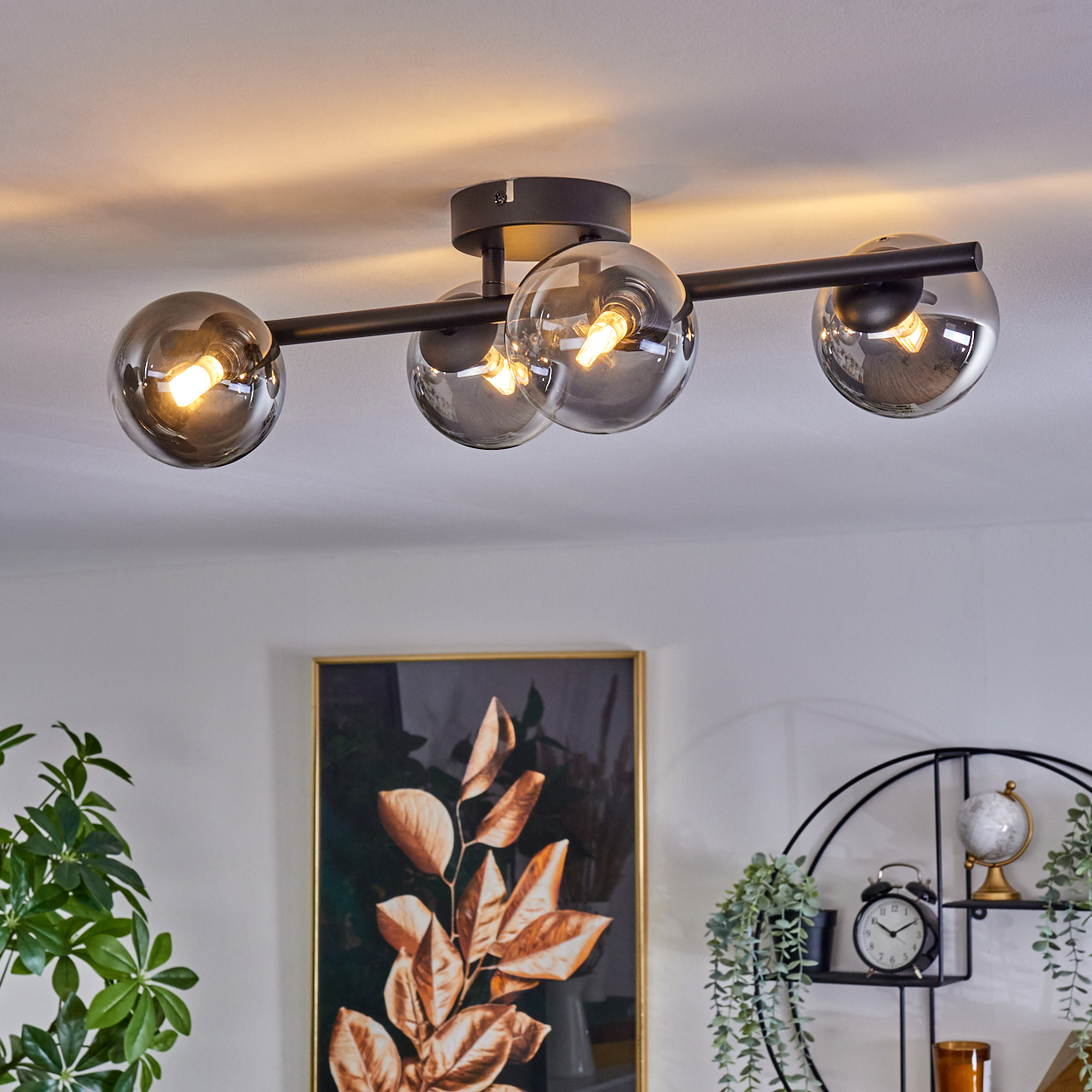 Eine an der Decke befestigte Leuchte mit vier rauchigen Glaskugel-Schirmen. Die Leuchte befindet sich in einem modernen Wohnraum.