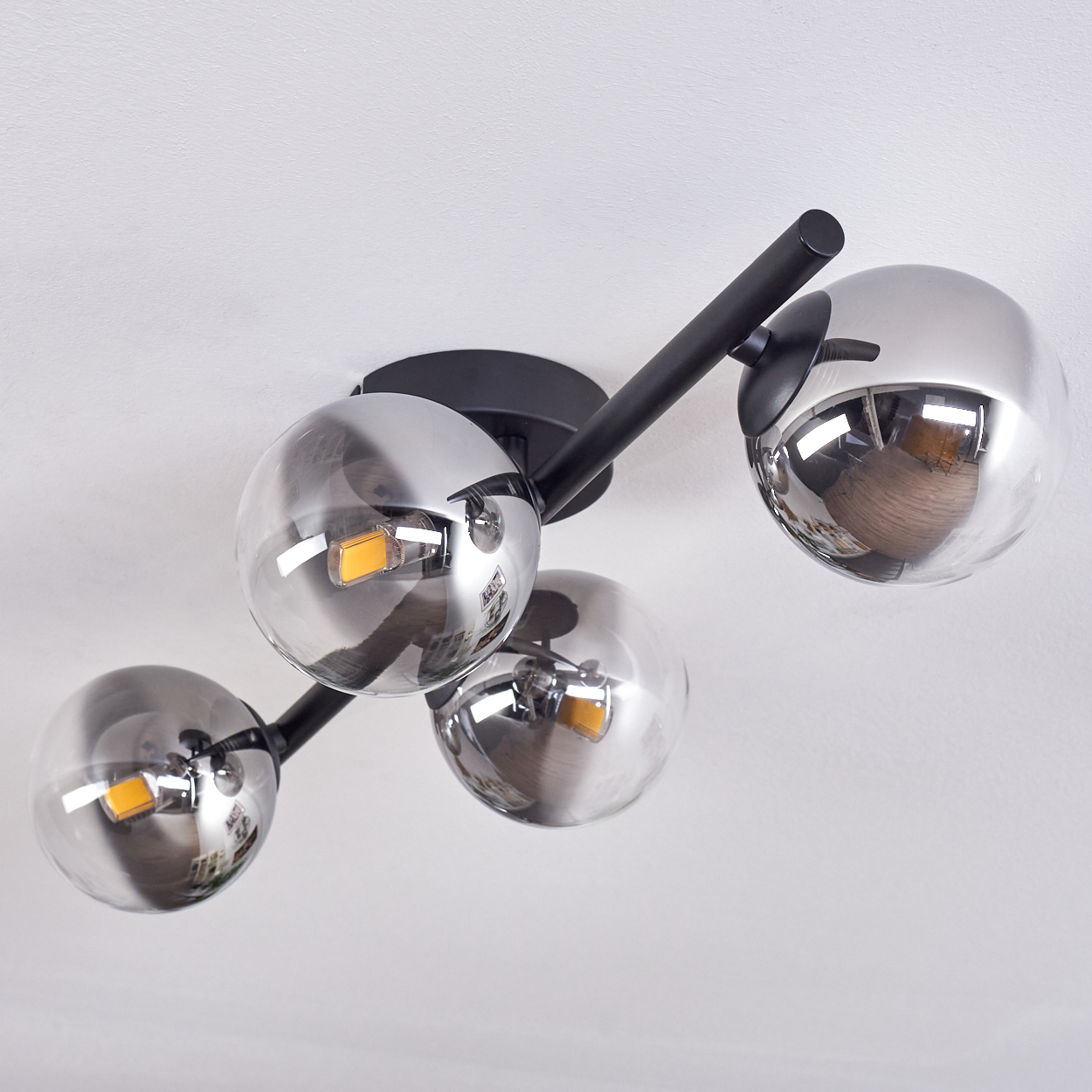 Leuchte mit vier kugelförmigen, rauchigen Glasschirmen. Die Leuchte ist mit einem Winkel an der Decke befestigt.