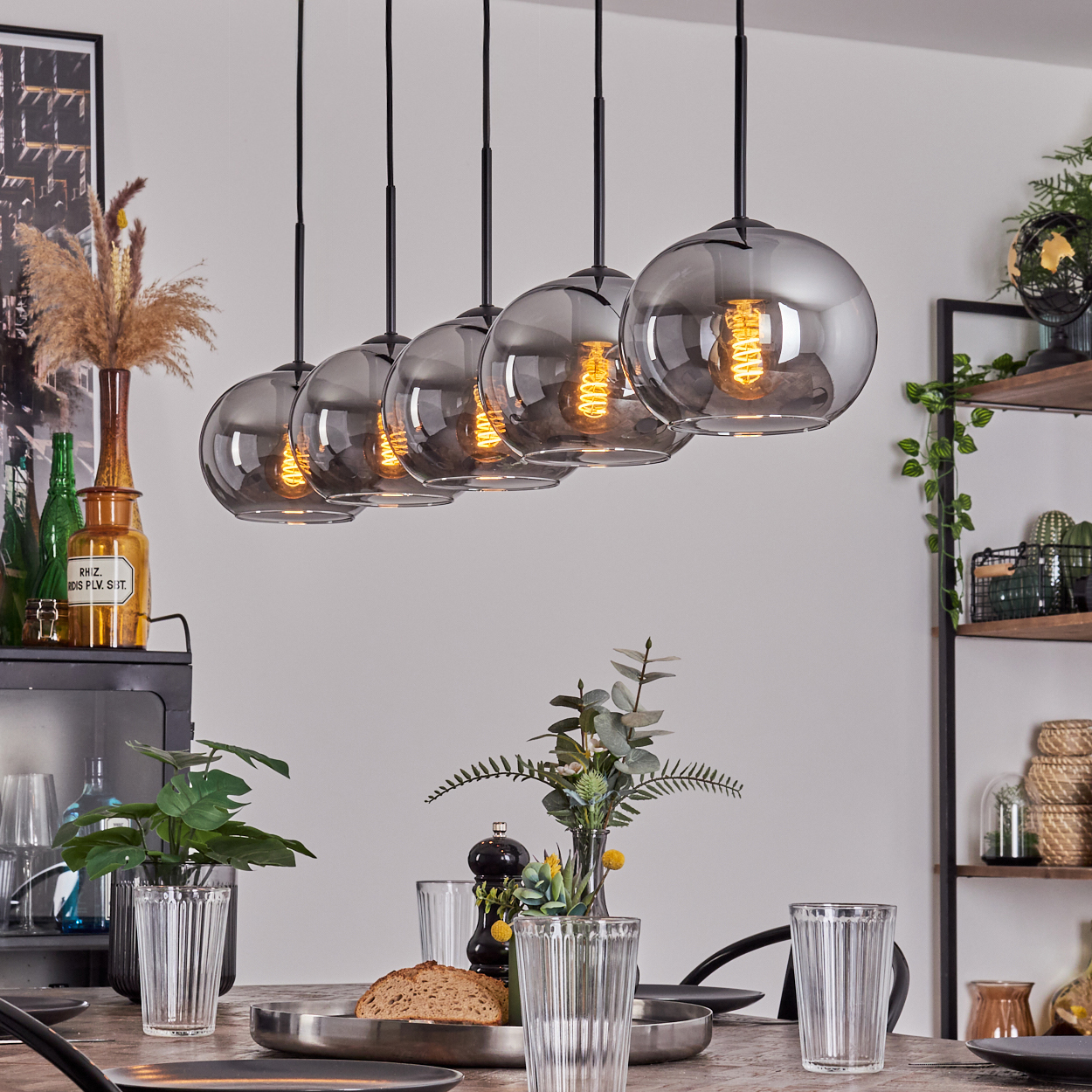 Ein Esszimmer mit Tisch, Pflanzen und fünf Hängeleuchten mit Glasschirmen.