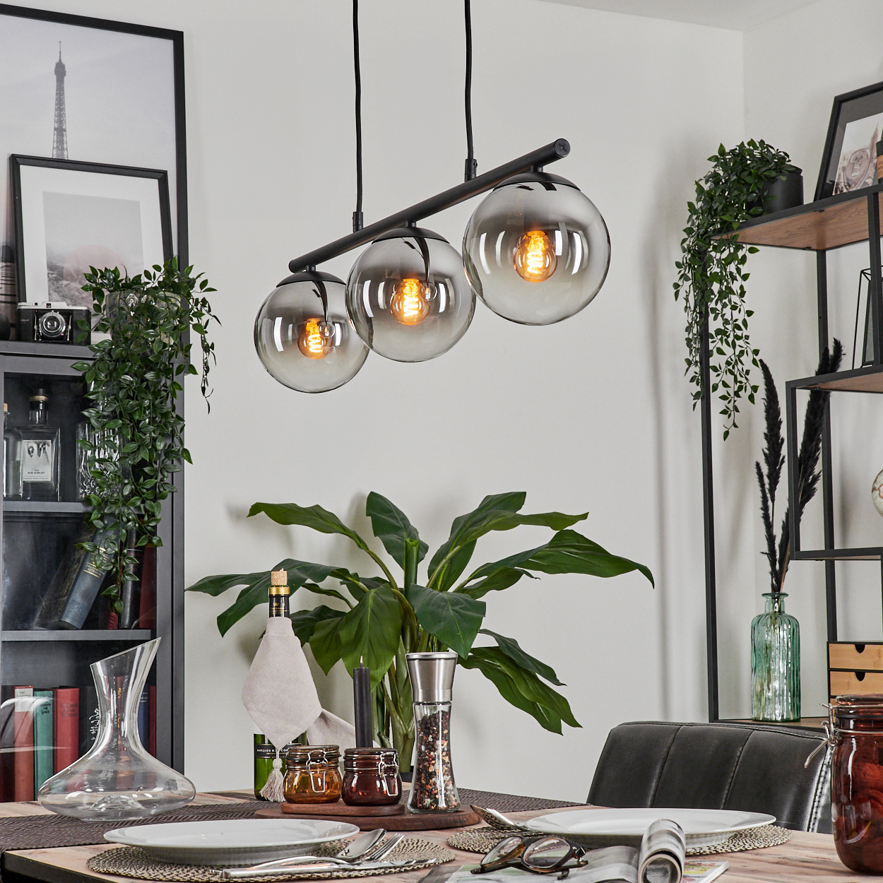 Ein Esszimmer mit Tisch, Pflanzen und drei Hängeleuchten mit Glasschirmen.