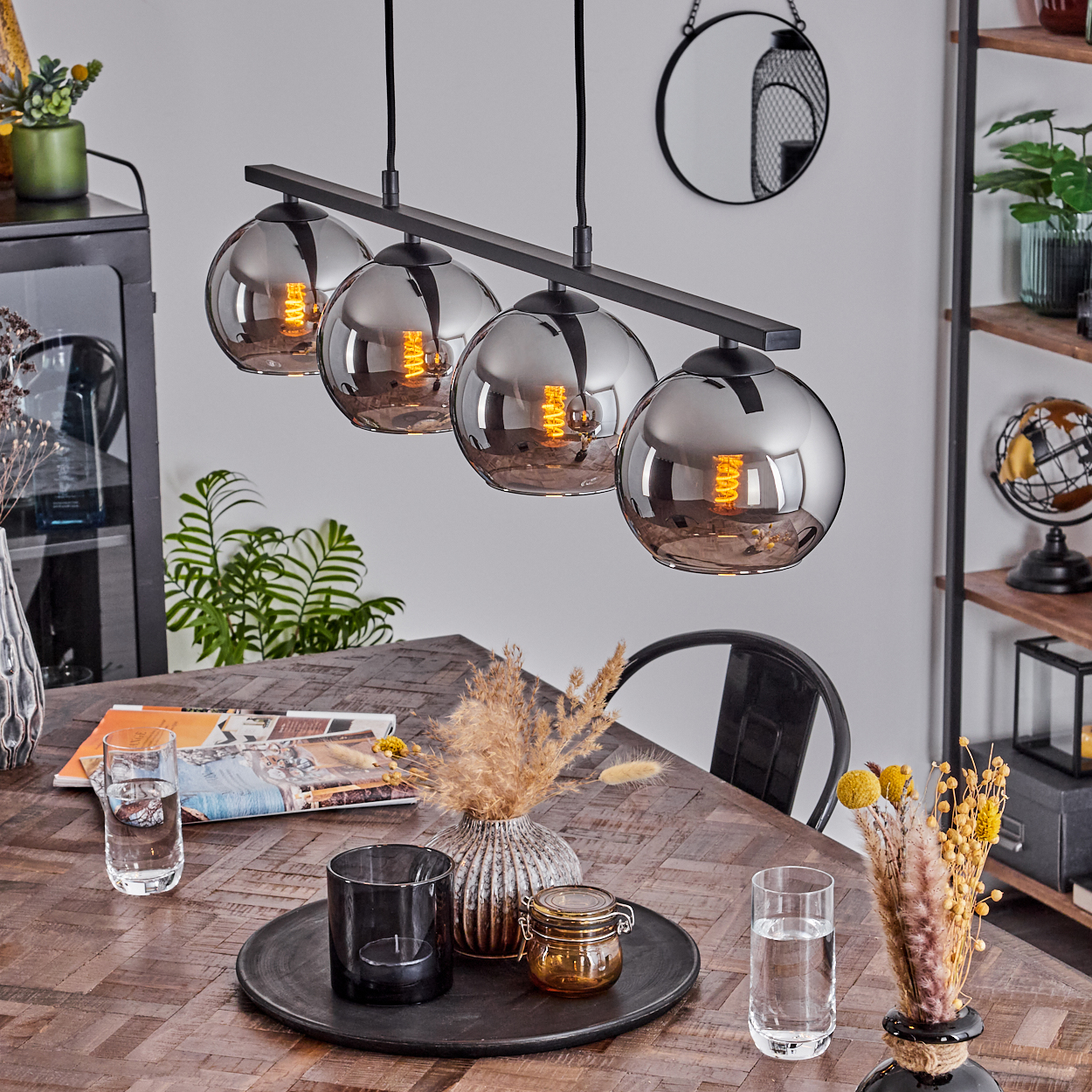 Esszimmer mit Holztisch, Dekorationsartikeln und vier Kugel-Pendelleuchten mit sichtbaren Glühbirnen.