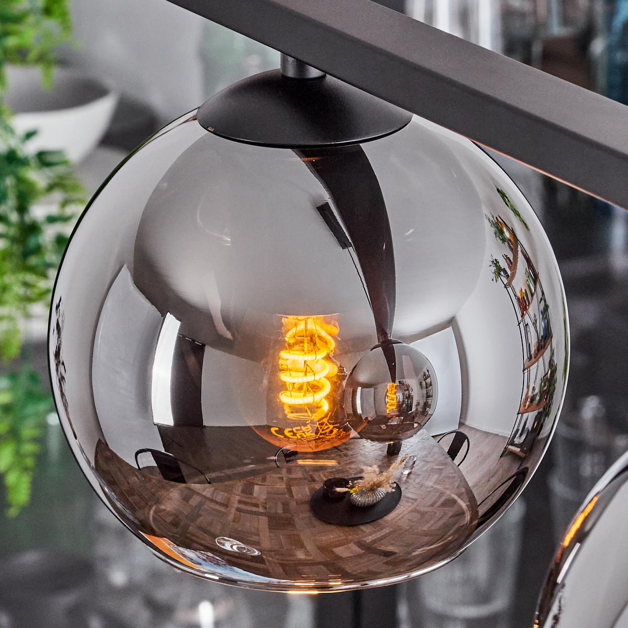 Nahaufnahme einer reflektierenden Kugel-Pendelleuchte mit sichtbarer Wendelglühbirne. Das Licht reflektiert den Raum.