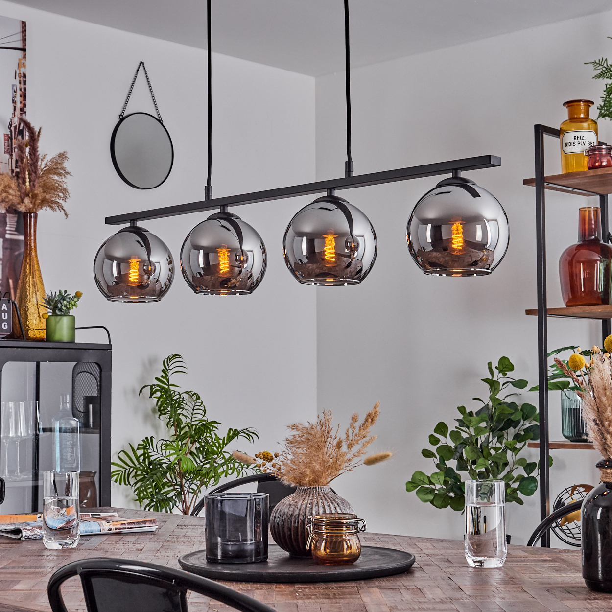 Esstisch mit vier kugelförmigen Pendelleuchten. Der Tisch ist mit Essen, Pflanzen und Gläsern gedeckt.