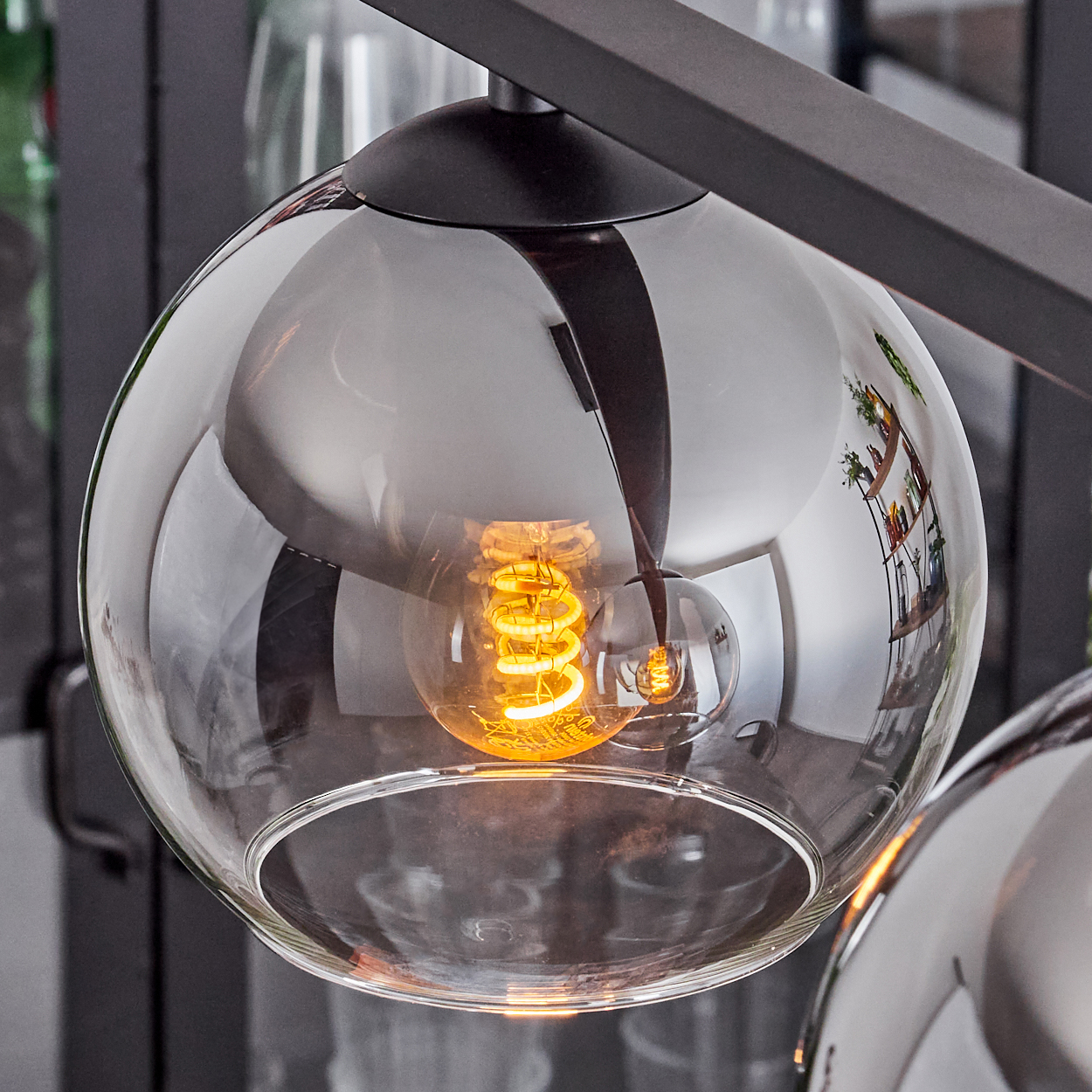 Nahaufnahme einer bauchigen Pendelleuchte mit klarem Glasschirm und sichtbarer Glühbirne.