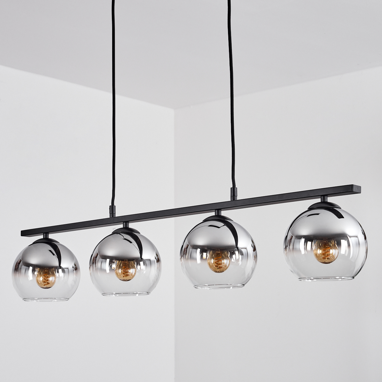 Vier Glaskugelleuchten, die an einer schwarzen Stange hängen. Die Lichter sind an.