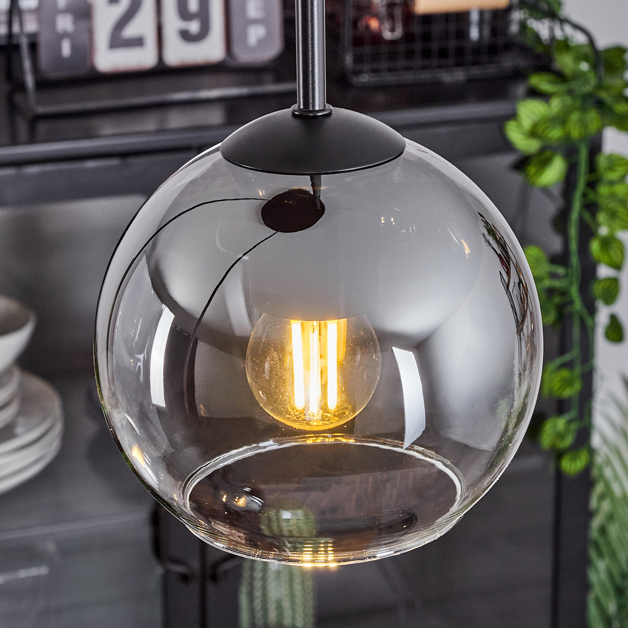 Nahaufnahme einer einzelnen Glaskugel-Pendelleuchte. Die Glühbirne im Inneren leuchtet.