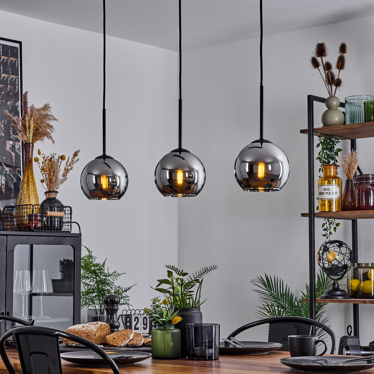 Esszimmer mit drei Glaskugel-Pendelleuchten. Tisch mit Brot, Pflanzen und Dekoration.