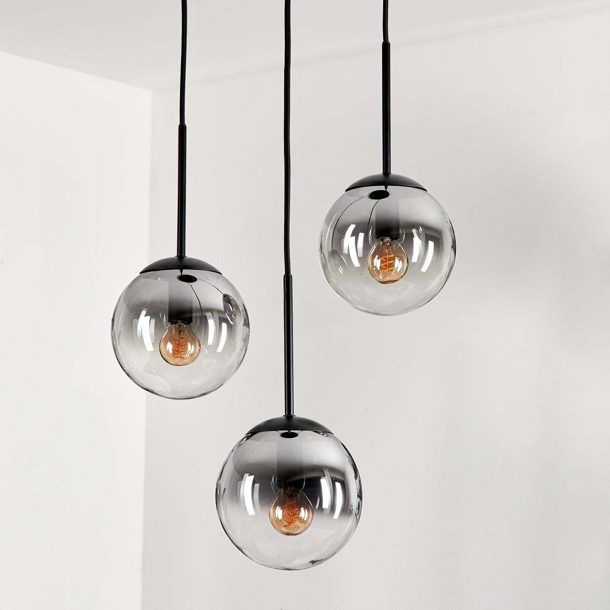 Drei Pendelleuchten mit rauchfarbenen Glaskugelschirmen und sichtbaren Glühbirnen hängen in einem Raum mit weißer Decke.