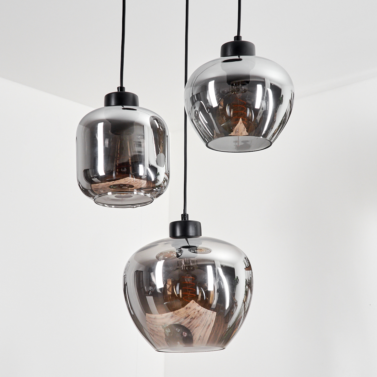Drei Pendelleuchten mit grauen, tropfenförmigen Glasschirmen, die von einer weißen Decke hängen.