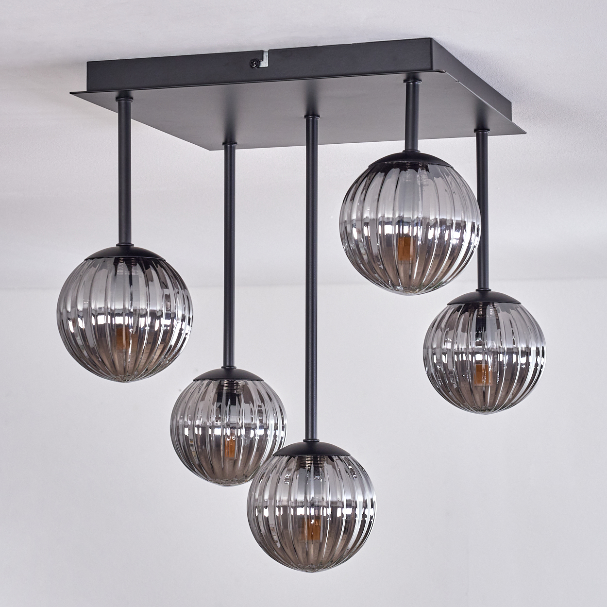 Fünf Pendelleuchten mit grauen, gerippten Glasschirmen, mit warmem Licht, hängen von einem schwarzen quadratischen Sockel.