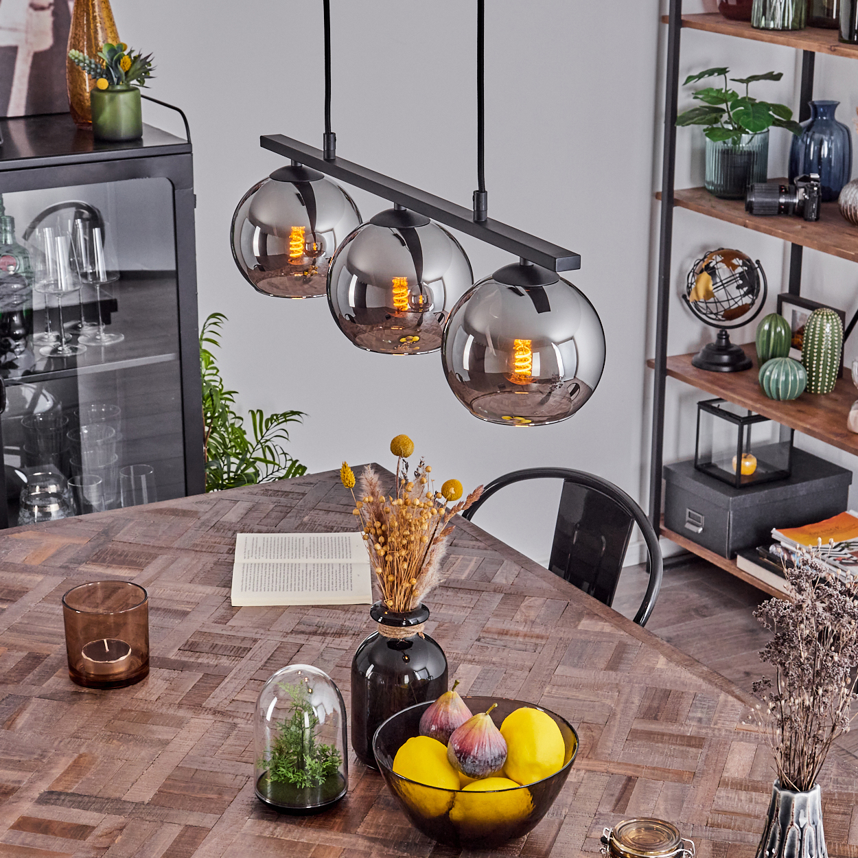 Esszimmer mit drei silbernen Kugelleuchten, Holztisch, Dekoration und Obstschale.