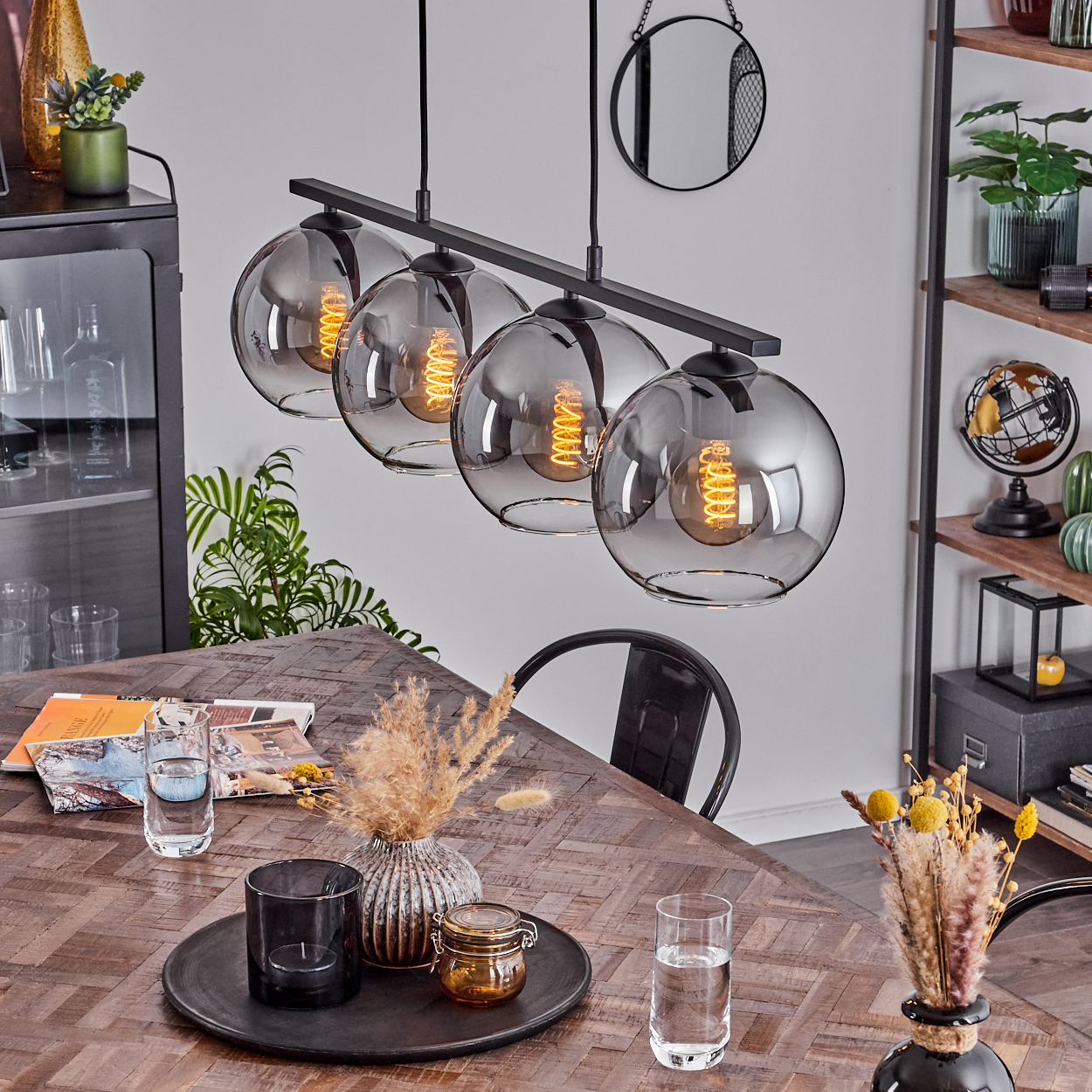 Esszimmer mit vier silbernen Kugelleuchten, einem Holztisch, Dekorationsartikeln und Pflanzen.