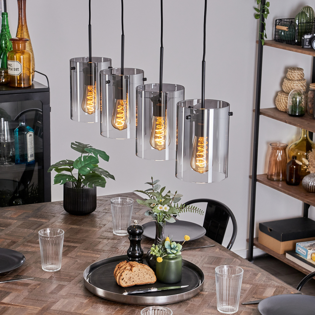 Esszimmer mit vier Glaszylinderleuchten, Holztisch, Dekorationsartikeln und Pflanzen.