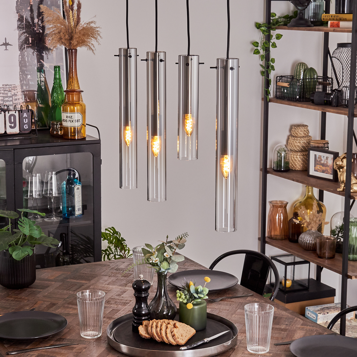 Esszimmer mit vier Glaszylinderleuchten, Holztisch und Dekoration.