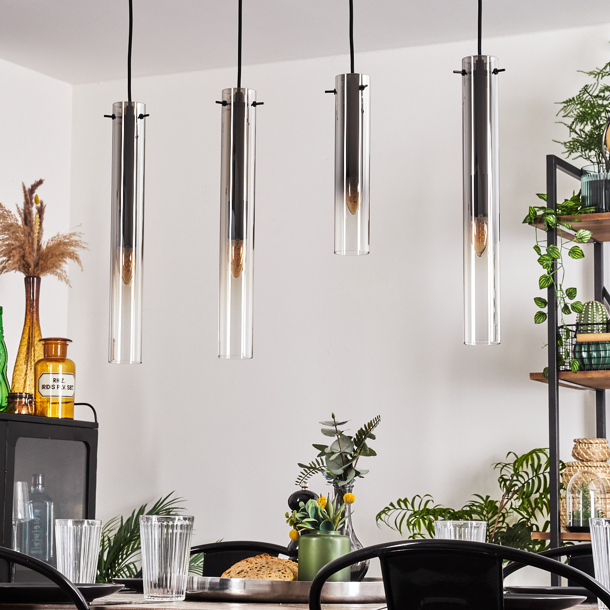 Esszimmer mit vier Glaszylinderleuchten, Holztisch, Dekoration und Pflanzen.