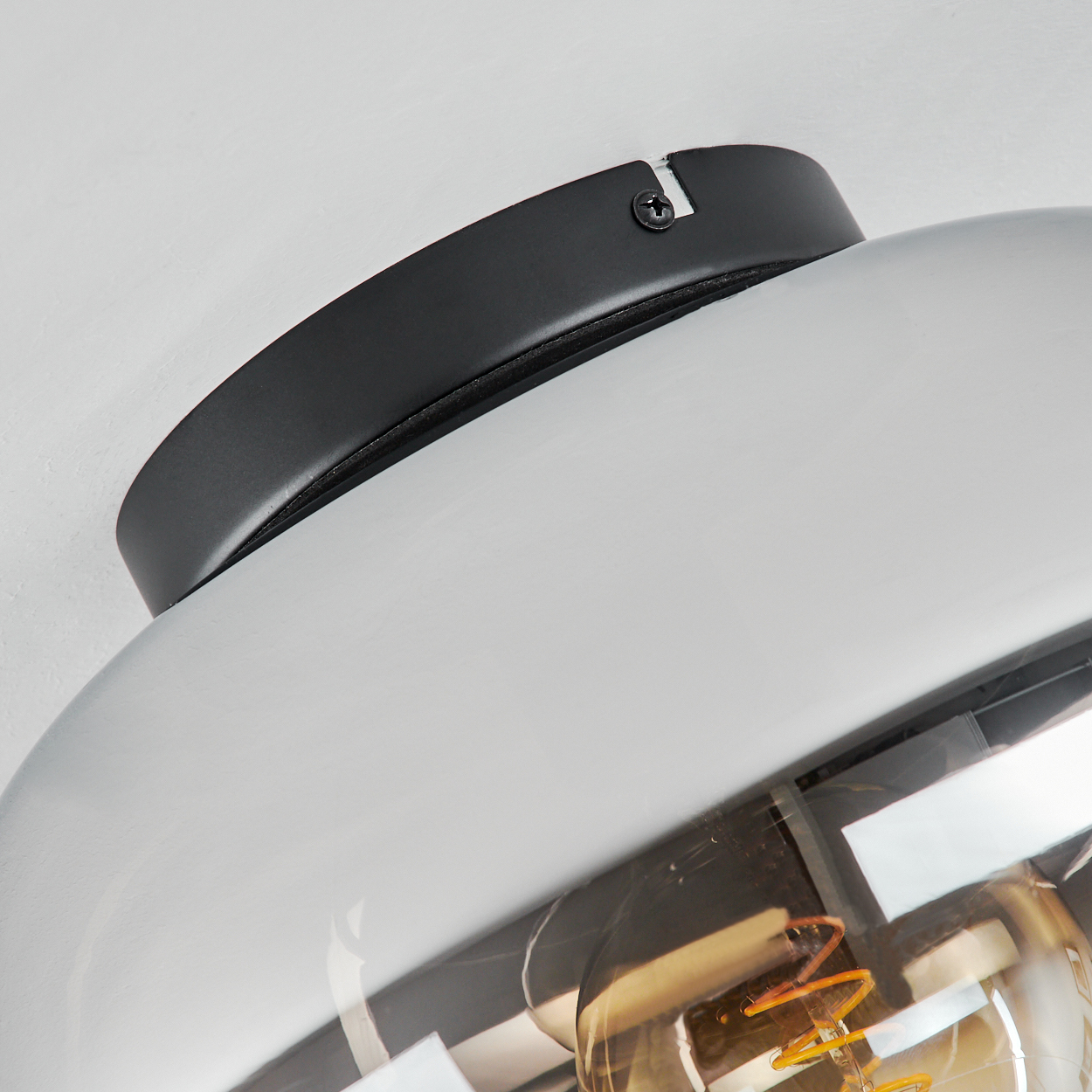 Nahaufnahme einer schwarzen Halterung, die an einer silbernen, bauchigen Lampe befestigt ist, mit einer sichtbaren Glühbirne.