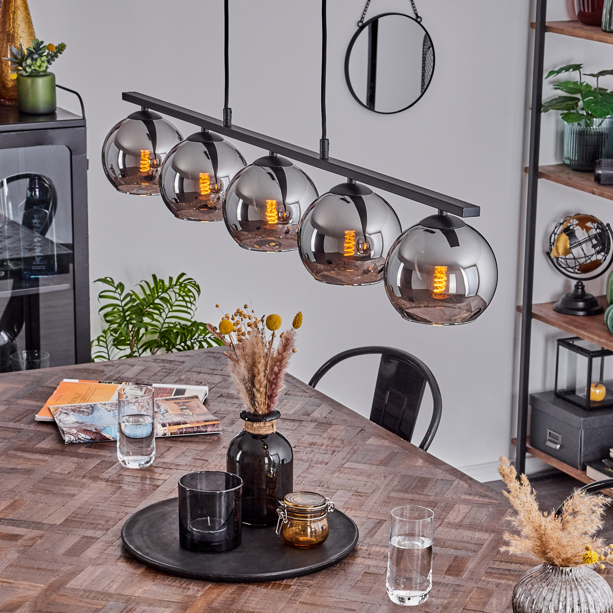 Fünf silberne Kugel-Pendelleuchten über einem Esstisch. Tisch mit Deko und Pflanzen. Spiegel an der Wand.