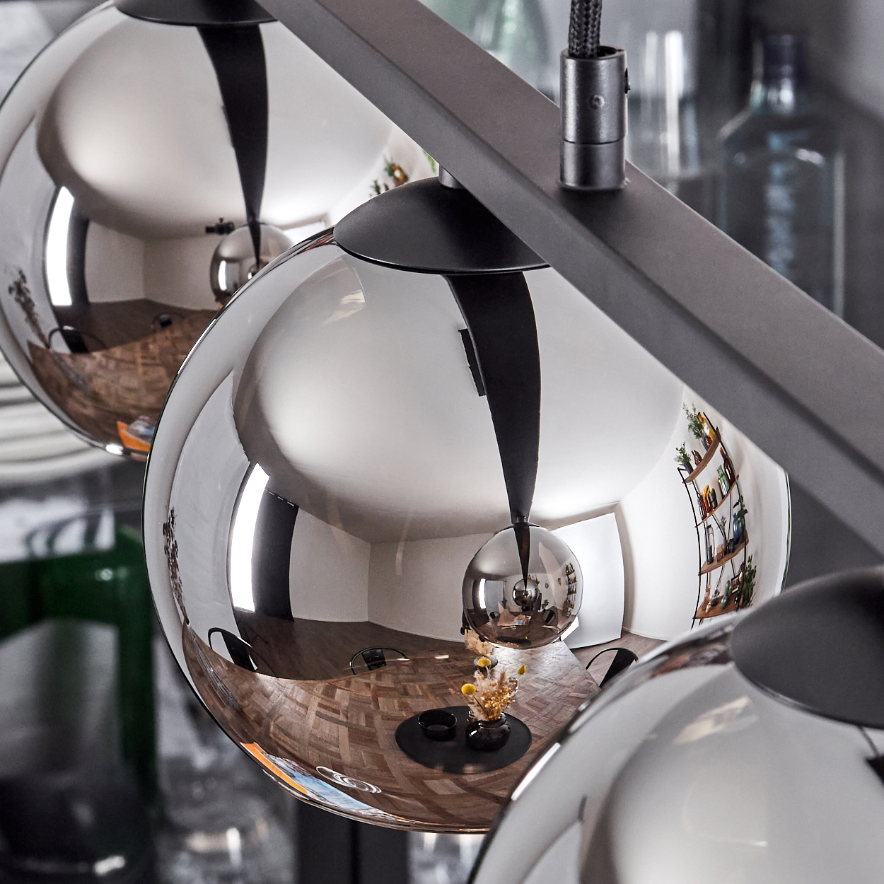 Nahaufnahme von drei Glaslampen, die einen Raum reflektieren. Die Lampen haben schwarze Armaturen. Dunkler Hintergrund mit Grüntönen.