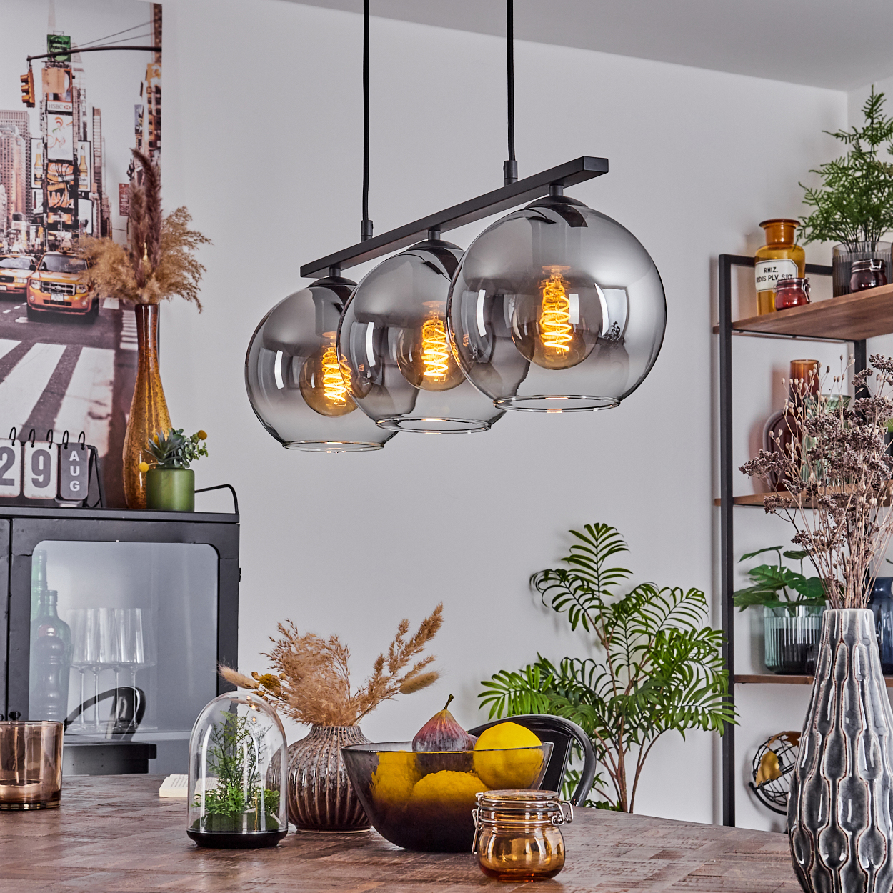 Esszimmer mit drei Hängeleuchten, einem gedeckten Tisch und dekorativen Gegenständen. Die Lichter sind an.