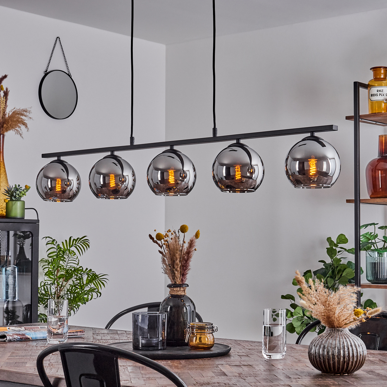 Eine Hängelampe mit fünf beleuchteten silbernen Kugelleuchten über einem Holztisch. Der Raum hat Dekorationen. Die Lampen haben schwarze Armaturen.